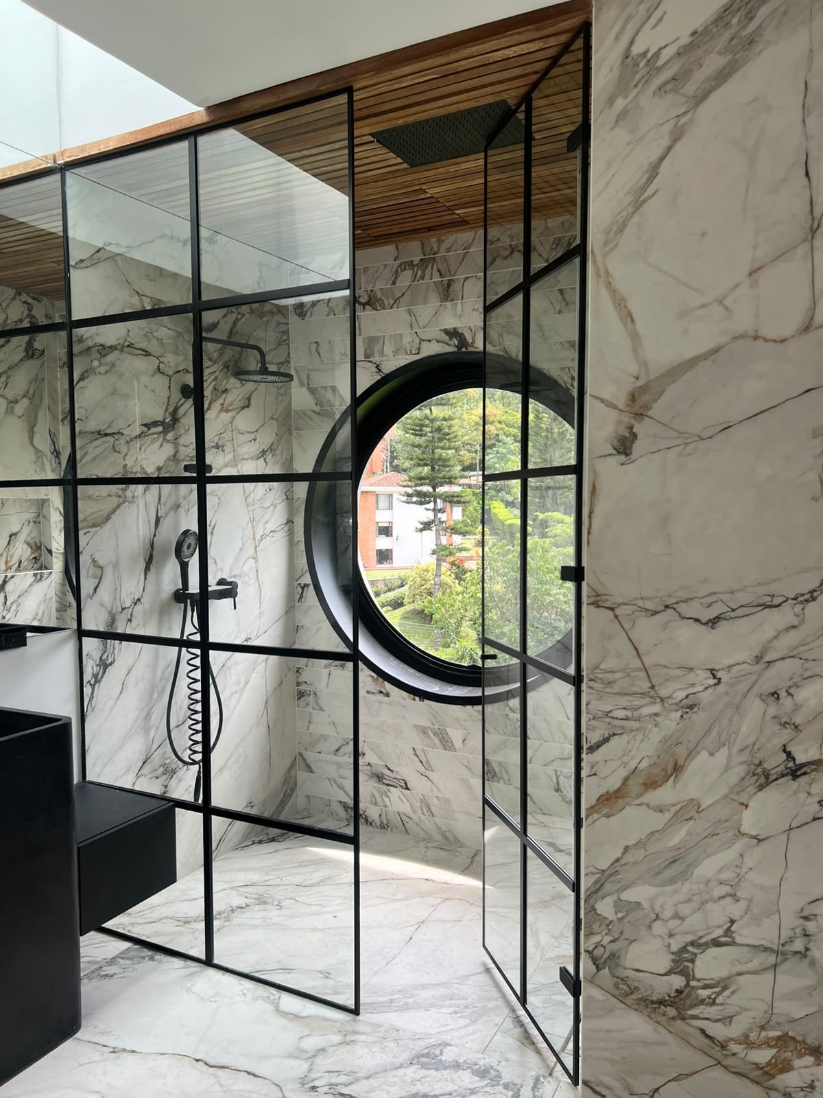 Cabina de baño en vidrio con perfiles negros y ventana redonda